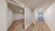 Located at 18807 8th Ave NE in Shoreline, Washington, this thoughtfully designed single-floor space offers a clean, modern aesthetic with high-quality finishes throughout. Light oak hardwood flooring runs continuously across the entire layout, creating a cohesive and airy feel.

The open-concept kitchen and living area serves as the heart of the space, featuring a well-appointed kitchen with warm wood upper cabinetry, gray lower cabinets, a tile backsplash, stainless steel appliances including a refrigerator, range, microwave, and dishwasher, and ample counter space. The kitchen flows seamlessly into a generous living area with exposed concrete ceiling accents, a ceiling fan, and large windows fitted with horizontal blinds that allow abundant natural light and outdoor views.

A corridor lined with sleek, floor-to-ceiling sliding panel doors leads to the private areas of the space, including a dedicated closet and a full bathroom. The bathroom is outfitted with a dual-sink vanity featuring a quartz countertop, a large mirror with overhead lighting, a bathtub, and in-unit laundry. An additional room with a stylish frosted-glass barn door offers flexible use. The overall ambiance is clean, contemporary, and move-in ready.