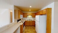 This single-floor residence offers a well-organized layout with a variety of functional spaces throughout. The kitchen is efficiently designed in a U-shaped configuration, featuring warm oak cabinetry that extends to the ceiling for generous storage, light-toned countertops, and a full suite of white appliances including a range, microwave, dishwasher, and refrigerator. Stone-patterned tile flooring anchors the kitchen and carries through into the bathroom, providing a cohesive, easy-to-maintain surface in high-use areas.

The living room is a comfortable, open space highlighted by a tile-surround gas fireplace that serves as a natural focal point. A ceiling fan with a light fixture overhead adds both function and a classic touch. The room also features a charming octagonal accent window that brings in natural light and adds architectural character. Baseboard heating runs along the walls throughout the living areas and bedrooms, ensuring consistent warmth.

The bedrooms are carpeted and clean, with neutral walls and ample natural light streaming through sliding windows that overlook outdoor greenery. The bathroom is practical and well-appointed, with tile flooring, oak vanity cabinetry, and a closet for additional storage. Overall, the space presents a straightforward, comfortable layout suited for everyday living.