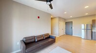Located at 353 Vine St in West Lafayette, Indiana, this thoughtfully designed 2-bedroom, 2-bathroom unit offers a contemporary and functional layout across a single floor. The open-concept living area is bright and welcoming, featuring light hardwood-style flooring, recessed lighting, and a ceiling fan. Large sliding glass doors lead to a private balcony, filling the space with natural light and offering outdoor views of the surrounding area. A wall-mounted TV and clean neutral tones complete the living room's modern aesthetic. The kitchen runs alongside the living area and is outfitted with warm wood cabinetry, white countertops, stainless steel appliances including a refrigerator, range, dishwasher, and built-in microwave, plus a single-basin sink. A closet near the entryway provides convenient storage. Both bedrooms are carpeted and offer a quiet, comfortable retreat, with the primary bedroom featuring a ceiling fan and a window with outdoor views. Each bathroom includes a full tub-shower combination with matte black fixtures and clean white surrounds. The unit also includes a dedicated laundry area, adding everyday convenience to this well-appointed West Lafayette residence.
