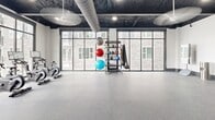 Located at 341 Great Circle Rd in Nashville, TN, this single-floor fitness center is a comprehensively equipped facility designed to support a wide range of workout styles. The space is defined by its industrial-modern aesthetic, featuring an exposed dark ceiling with visible ductwork, structural beams, and recessed lighting complemented by large ceiling fans that ensure airflow throughout the facility.

The main cardio zone is generously sized and lined with floor-to-ceiling windows that invite abundant natural light and offer views of the surrounding outdoor amenities, including a pool area. This section houses a full lineup of TRUE-brand treadmills, ellipticals, stationary bikes, and rowing machines. A dedicated cycling studio with spin bikes and wall-mounted displays provides a focused group or individual training environment, also benefiting from expansive window views.

A functional training area offers open floor space for dynamic workouts, equipped with a multi-station cable and rack system, kettlebell racks, medicine balls, stability balls, resistance bands, and a flat bench. An additional open flex zone provides space for stretching or group exercise. Durable rubberized flooring spans the facility, and decorative glass-panel doors with artistic accents add a refined touch. The overall ambiance is bright, spacious, and purpose-built for serious fitness.
