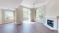 This thoughtfully designed residence offers a comfortable and functional layout spread across multiple levels, connected by a carpeted staircase with a classic white handrail and trim. The open-concept living area is a standout, featuring rich hardwood-style flooring, vaulted ceilings, and a ceiling fan overhead. A white marble-surround fireplace serves as a focal point, while large windows and a sliding glass door flood the space with natural light and provide direct access to an outdoor deck overlooking lush greenery. The kitchen is well-equipped with white shaker-style cabinetry, stainless steel appliances including a French door refrigerator and microwave, light quartz countertops, and a breakfast bar peninsula ideal for casual dining. The bedrooms offer plush carpeting, generous windows with vertical blinds, and baseboard heating for year-round comfort. The bathroom is clean and functional, featuring a white vanity with undermount sink, a tiled shower-tub combination, and ample mirror storage. Neutral warm-toned walls throughout the space create a cohesive and inviting atmosphere. Dark hardwood-style flooring in the main living areas contrasts elegantly with the light cabinetry and walls, lending the space a modern yet welcoming character.
