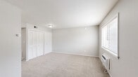 This one-bedroom, one-bathroom unit at 4415 Oakwood Blvd in Melvindale, Michigan offers a practical and efficient single-floor layout. The open living area flows directly into the kitchen, which is equipped with gray cabinetry, a white range, a refrigerator, and a single-basin sink beneath a window. The transition from carpet in the living area to hard-surface flooring in the kitchen creates a clear visual distinction between the two zones. Neutral gray walls and white trim are consistent throughout, lending a clean, cohesive aesthetic. The spacious bedroom features plush carpeting, a window that allows natural light to filter in, and a double sliding-door closet offering ample storage. A second carpeted room with its own window provides additional flexibility. The full bathroom is finished with light tile flooring, a gray vanity with a marble-style countertop and brushed nickel hardware, a well-lit mirror, a toilet, and a full tub-shower combination with white tile surround. The unit's straightforward layout and neutral palette make it a versatile and move-in-ready space.