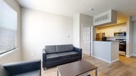 This single-floor unit in Stillwater, Oklahoma presents a clean, contemporary layout designed for comfortable everyday living. The open-concept living area is bright and welcoming, featuring light wood-look flooring, neutral white walls, and large windows fitted with blinds that allow for ample natural light. The space accommodates a full seating arrangement and coffee table, creating a functional gathering area.

The galley-style kitchen is well-appointed with white shaker cabinetry, dark granite-style countertops, and stainless steel appliances including a refrigerator, dishwasher, and range. A pass-through opening connects the kitchen to the living area, enhancing the open feel. A utility closet with in-unit laundry hookups is accessible directly from the kitchen.

Both bedrooms are carpeted and modestly sized, each featuring a ceiling fan and window with blinds for natural light and ventilation. The two bathrooms mirror each other in design, showcasing white shaker vanities with dark granite countertops, white subway-tiled tub-shower combinations accented with a black tile border, and warm wood-look flooring. One bathroom includes an LED-backlit vanity mirror, adding a modern touch to the overall aesthetic.