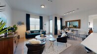 This well-appointed single-floor residence showcases a thoughtfully designed open-concept layout that seamlessly connects the living, dining, and kitchen areas. The living room is a standout space, anchored by large windows with wood-slat blinds and floor-to-ceiling teal drapes that flood the room with natural light. Track lighting and a dedicated dining area with a rustic wood-framed mirror add character and functionality.

The kitchen features sleek gray cabinetry, stainless steel appliances, a subway tile backsplash, and a generous quartz island with bar seating illuminated by pendant lighting — ideal for both cooking and entertaining.

Two bedrooms offer comfortable retreats, each with large windows, light wood-look flooring, and ample space for furnishings. One bedroom presents a vibrant, eclectic aesthetic, while the second maintains a calm, minimalist feel.

Two bathrooms mirror the home's clean design aesthetic, finished with white quartz vanities, white tile surrounds, and tub-shower combinations. Light wood-look flooring runs consistently throughout the unit, tying the spaces together with a cohesive, modern sensibility. Overall, the residence balances contemporary style with warm, inviting touches.