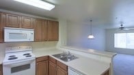 This single-floor residence at 2050 Key70 offers a practical and comfortable layout designed for everyday living. The kitchen is a standout feature, showcasing warm medium-toned wood cabinetry that provides generous storage space above and below the countertops. Light-colored counters run along the L-shaped workspace, offering ample room for meal preparation. White appliances, including a range and dishwasher, are seamlessly integrated into the design, complemented by a built-in microwave. A double basin sink is positioned beneath a pass-through opening, which connects the kitchen to the adjacent dining or living area, enhancing the sense of openness and allowing natural interaction between spaces. A pendant light fixture hangs elegantly over the pass-through, adding a warm focal point to the transition between rooms. Overhead fluorescent lighting in the kitchen ensures a bright and functional workspace. The light-toned walls throughout contribute to an airy, clean ambiance. The single-floor layout promotes ease of movement and accessibility throughout the unit, making the space efficient and well-suited for comfortable day-to-day living.