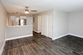 This single-floor unit features a cohesive, modern aesthetic carried throughout by warm wood-look luxury vinyl plank flooring. The open-concept living and dining area is anchored by a ceiling fan with integrated lighting and flows seamlessly toward the kitchen, which is separated by a low breakfast bar with slatted paneling. The kitchen is equipped with stainless steel refrigerator, white cabinetry, and a sink positioned beneath upper shelving, offering a functional and clean workspace.

A dedicated bedroom provides a quiet retreat, featuring a window with exterior views, a wall-mounted air conditioning unit, and baseboard heating — ensuring year-round climate control. Generous closet space is accessible via double doors off the main living area, adding practical storage.

The full bathroom is finished in a crisp, all-white palette with a single-sink vanity featuring clean-lined white cabinetry, a framed mirror, chrome fixtures, and a full-size soaking tub with an overhead shower. Wood-look flooring extends into the bathroom, maintaining design continuity. The overall ambiance is neutral, clean, and move-in ready, suited for straightforward, comfortable everyday living.
