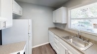 This single-floor home offers a clean, move-in-ready interior finished in a cohesive cool gray palette throughout. The main living area features durable wood-look laminate flooring, crown molding, and a classic chair rail detail along the walls, adding a touch of architectural character. Natural light enters generously through blinds-fitted windows, and a front entry door with a transom window provides additional brightness. A bifold closet door adds practical storage within this space.

The kitchen is efficiently laid out with white cabinetry, speckled laminate countertops, a stainless steel sink, and white appliances including a refrigerator and dishwasher. A window above the counter allows natural light into the workspace.

Multiple bedrooms share a consistent design: soft neutral carpet, gray walls, and windows with blinds that invite outdoor views and natural light. Ceiling fans with light fixtures are present in several rooms, contributing to comfort and functionality. One bedroom includes a door leading to an adjacent space, offering added convenience.

The bathroom features a full-size soaking tub with an overhead shower, a curved curtain rod, chrome fixtures, and a window for ventilation and natural light, completing this practical and well-appointed home.
