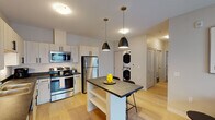 This single-floor residence at Prairie Pkwy SW in Wyoming, Michigan offers a well-designed layout with a clean, contemporary aesthetic throughout. The open-concept kitchen serves as the heart of the home, outfitted with stainless steel appliances including a range, microwave, refrigerator, and dishwasher. Light-toned shaker-style cabinetry with matte black hardware pairs with dark countertops for a modern contrast, while light hardwood-style flooring adds warmth to the space. A central kitchen island with seating provides additional workspace and casual dining. Pendant lighting overhead adds a stylish finishing touch. A stacked washer and dryer unit is conveniently located just off the kitchen area. The bedroom is generously proportioned, featuring plush carpeting, a large window that invites natural light, and ample wall space for personalization. A flexible secondary room, also carpeted and naturally lit, functions well as a home office or den and includes its own window and closet access. The bathroom is finished with a wood-toned vanity, white countertop, and tile flooring, maintaining the residence's cohesive modern palette. Neutral wall tones and thoughtful lighting choices throughout create a bright, inviting ambiance suited for comfortable everyday living.