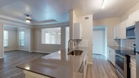 This single-story residence is designed with a modern, open-concept layout that promotes a cohesive flow between the kitchen, dining, and living areas. The kitchen serves as a central hub, featuring a peninsula with a dark quartz-style countertop, an undermount sink, and a full suite of stainless steel appliances including a refrigerator, range, and microwave. White shaker-style cabinetry pairs with a classic subway tile backsplash, providing a clean and contemporary aesthetic. Track lighting overhead ensures the workspace is well-illuminated.

The adjoining living area benefits from a large window that draws in natural light, creating a bright and welcoming atmosphere. Crown molding and a tray ceiling detail add architectural interest, while a pendant chandelier provides an elegant focal point. Wood-look plank flooring runs consistently throughout the main living spaces and bedrooms, contributing to a unified, modern feel.

The bedrooms are comfortably sized, each featuring neutral-toned walls, wood-look flooring, and windows with blinds that allow for natural light and privacy. The bathrooms are finished with white vanity cabinetry, gray countertops, undermount sinks, and brushed nickel hardware, reflecting a clean, functional design throughout.