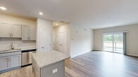 Located at 33451 Mackenzie Way in Lewes, Delaware, this single-floor residence offers a well-designed, contemporary living environment. The open-concept layout connects the kitchen and living area seamlessly, creating a bright and welcoming atmosphere throughout.

The kitchen is a standout feature, equipped with stainless steel appliances including a refrigerator, range, microwave, and dishwasher. Grey shaker-style cabinetry pairs elegantly with granite countertops, while a central island provides additional workspace and casual dining. Recessed lighting illuminates the space efficiently.

The living area is generously proportioned, featuring light-toned hardwood-style flooring and neutral walls that lend a clean, modern feel. Sliding glass doors open to a private balcony overlooking a scenic outdoor setting with greenery and a pond view, allowing natural light to pour in.

The bedrooms are carpeted for comfort and feature large windows that bring in views of the surrounding landscape. Each room connects conveniently to well-appointed bathrooms, one featuring a walk-in shower with brushed nickel fixtures, and another offering a full tub-shower combination. Both bathrooms continue the neutral color palette with hardwood-style flooring and clean white vanities.