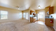 This single-floor residence offers a practical and well-organized layout designed for comfortable everyday living. The open living area is generously proportioned, finished with neutral-toned carpeting and warmed by natural light streaming through multiple windows and a glass-paneled exterior door. A ceiling fan provides added comfort, and the space transitions seamlessly into a kitchenette area near the entry, equipped with warm wood cabinetry, a sink, and a refrigerator.

The dedicated galley-style kitchen is efficiently designed with wood-toned cabinetry lining both sides, ample counter space, a double sink, a full-size refrigerator, and a white electric range with overhead ventilation — all set on durable hardwood-style flooring.

The bedrooms are carpeted and bright, each featuring a ceiling fan and windows that allow natural light. The primary bedroom connects directly to a vanity area with a wood-framed sink cabinet and a large mirror, alongside a spacious walk-in closet fitted with wire shelving for organized storage.

Two full bathrooms serve the unit, each featuring a tub-shower combination, toilet, wood-toned cabinetry, and hardwood-style flooring. The overall color palette throughout the unit is light and neutral, creating a clean, welcoming atmosphere.