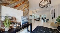 Located at 11410 Esplanade Dr in Reston, VA, this beautifully appointed community clubhouse offers a refined and welcoming atmosphere across a thoughtfully designed single-floor layout. The entry foyer makes an immediate impression with a striking reclaimed wood accent wall, decorative globe chandelier, and curated artwork, setting the tone for the spaces beyond.

The main lounge is a standout area, featuring soaring ceilings, dramatic arched windows that flood the space with natural light, and a floor-to-ceiling tiled fireplace with a mounted flat-screen TV. Light wood-look tile flooring flows throughout, complementing the contemporary furnishings and open, airy feel.

Adjacent to the lounge, a modern kitchenette is outfitted with gray shaker cabinetry, a bold navy herringbone tile backsplash, quartz countertops, and a large arched window overlooking lush greenery. A sunroom with exposed brick knee walls and expansive floor-to-ceiling windows provides a serene gathering space with rustic wood furnishings and sweeping outdoor views.

The dining area features a live-edge wood table surrounded by velvet chairs, accented by a gallery wall of botanical prints. The fitness center is comprehensively equipped with treadmills, an elliptical, a stationary bike, free weights, resistance equipment, wall-mounted TVs, and full-length mirrors. A water station and community bulletin board complete the functional amenities of this polished clubhouse.