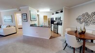 This single-floor residence offers a thoughtfully designed open-concept layout that seamlessly connects the kitchen, dining, and living areas. The kitchen is outfitted with white cabinetry, dark granite countertops, stainless steel appliances including a range, microwave, and refrigerator, and hardwood flooring that extends through the main cooking and dining zones. A peninsula with a sink provides additional prep space and serves as a natural divider between the kitchen and the adjacent carpeted living and dining areas.

The dining area accommodates a four-seat round table and is accented by crown molding that carries throughout the main living spaces, adding a refined touch. The living room is generously sized, featuring plush carpet, a ceiling fan, and windows fitted with blinds that allow for controlled natural light. French doors provide additional access to the exterior.

The bedroom is a comfortable retreat with carpet, a ceiling fan, and direct access to a full bathroom. The bathroom features a white vanity with a sink, a mirror with lighting, a soaking tub with tile surround, and hardwood flooring. A spacious walk-in closet with wire shelving provides ample storage, and a secondary walk-in closet with rod shelving serves the bedroom as well.