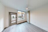 Located at 312 W Republican St in Seattle's Queen Anne neighborhood, this efficiently designed single-floor studio makes smart use of every square foot. The living area is bright and airy, featuring light wood-look flooring, crisp white walls, a ceiling fan with integrated lighting, and large windows that frame views of the private outdoor patio. A distinctive exposed concrete accent column adds an industrial touch, creating visual contrast against the clean, neutral palette. Direct access to the patio is provided through a glass-panel door, opening onto a landscaped outdoor space enclosed by concrete walls topped with natural wood slat fencing. Built-in planters with manicured shrubs and ground cover plantings give the patio a polished, low-maintenance feel. The galley-style kitchen is thoughtfully laid out with white cabinetry, open shelving, a smooth cooktop, under-cabinet range hood, and ample counter space. A stainless steel refrigerator and microwave complete the setup. The bathroom features a shower/tub combination with chrome fixtures and wood-look tile flooring. A dedicated closet provides additional storage. Recessed lighting and an accessible electrical panel are integrated throughout, reflecting a modern, functional design approach well-suited to urban living.