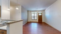 Located at 18-26 S Bedford St in the heart of Madison, WI, this 2-bedroom, 2-bathroom unit offers a well-designed single-floor layout making efficient use of its space. The kitchen is a standout feature, showcasing warm wood cabinetry, granite countertops, a peninsula with pendant lighting overhead, and black appliances including a refrigerator, range, and built-in microwave. Hardwood-style flooring extends through the kitchen and living areas, lending warmth and continuity throughout. The primary bedroom is a comfortable size and features hardwood-style flooring and a large window that brings in natural light. The second bedroom is carpeted and benefits from two tall windows with views of the surrounding neighborhood, providing a bright and airy feel. Both bathrooms are finished with tile flooring and granite-topped vanities with wood cabinetry. The primary bath includes a soaking tub, while the second bath features a glass-enclosed walk-in shower. The unit enjoys a lively urban setting, with street-facing windows offering views of the active South Bedford Street corridor and easy access to Madison's vibrant downtown amenities.