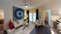 This single-floor residence is thoughtfully designed with a cohesive contemporary aesthetic throughout. The living room serves as a central gathering space, featuring dark hardwood-style flooring, crown molding, and a ceiling fan. A set of French doors with slatted blinds and floor-to-ceiling navy drapes allows natural light to filter in while adding a refined touch. The kitchen is a standout feature, showcasing two-tone cabinetry — crisp white lower cabinets paired with deep navy upper cabinets — complemented by granite countertops, subway tile backsplash, under-cabinet lighting, and a full suite of stainless steel appliances. A curved breakfast bar provides additional seating. An adjacent dining area offers space for a full dining set. The bedrooms are comfortably sized, each with plush carpeting and ample natural light. One bedroom features a large walk-in closet with multi-tiered wire shelving. The bathroom includes tile flooring, a granite-topped vanity, and neutral gray walls. A dedicated in-unit laundry room houses a full-sized washer and dryer with overhead shelving, adding everyday convenience to this well-rounded residence.