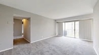 Located at 3822 Regency Pkwy in Suitland, MD, this single-floor unit offers three bedrooms, two bathrooms, and a practical layout designed to maximize functionality. The space is organized around two living areas, connected by hallways that provide clear separation between the common and private zones of the home.

The main living area is generously proportioned, featuring neutral gray carpeting, soft gray walls, and large sliding glass doors that open to a private balcony, flooding the room with natural light and providing outdoor views. A second living area offers additional flexible space, also finished with carpet and accessing the rest of the unit through two doorways.

The three bedrooms are carpeted and feature windows that bring in natural light; the primary bedroom is notably spacious with a tray ceiling detail and a large window overlooking green outdoor space. The kitchen is equipped with warm-toned wood cabinetry, dark granite-style countertops, a stainless steel sink, and a gas range, with wood-look vinyl flooring that extends into both bathrooms. Each bathroom features a tiled tub-shower combination, with one bath also offering a vanity area with countertop space. The entrance leads directly into the kitchen corridor, providing a smooth transition into the home.