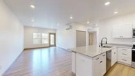 Located at 102 E Farwell in Spokane, WA, this well-designed 3-bedroom, 1-bathroom unit offers a clean, modern aesthetic throughout its single-floor layout. The open-concept living and kitchen area serves as the heart of the home, anchored by a large kitchen island with a quartz countertop, undermount sink, and matte black fixtures. White shaker cabinetry pairs with stainless steel appliances — including a refrigerator, range, and microwave — to create a functional and contemporary kitchen. Light hardwood flooring flows seamlessly throughout the entire unit, enhancing the bright, airy feel. Recessed lighting and a wall-mounted mini-split system are present in the main living area, which opens to an outdoor balcony access door framed by large windows that invite natural light and views of surrounding mature trees. Each bedroom is well-proportioned, with the spacious primary bedroom offering generous closet space, including a walk-in closet with wire shelving. The secondary bedrooms feature large windows with pleasant outdoor views. The bathroom is outfitted with a walk-in shower, a white vanity with storage, a round mirror, and matte black hardware accents, maintaining the unit's consistent modern design language.
