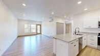 Located at 102 E Farwell in Spokane, WA, this well-designed 3-bedroom, 1-bathroom unit offers a clean, modern aesthetic throughout its single-floor layout. The open-concept living and kitchen area serves as the heart of the home, anchored by a large kitchen island with a quartz countertop, undermount sink, and matte black fixtures. White shaker cabinetry pairs with stainless steel appliances — including a refrigerator, range, and microwave — to create a functional and contemporary kitchen. Light hardwood flooring flows seamlessly throughout the entire unit, enhancing the bright, airy feel. Recessed lighting and a wall-mounted mini-split system are present in the main living area, which opens to an outdoor balcony access door framed by large windows that invite natural light and views of surrounding mature trees. Each bedroom is well-proportioned, with the spacious primary bedroom offering generous closet space, including a walk-in closet with wire shelving. The secondary bedrooms feature large windows with pleasant outdoor views. The bathroom is outfitted with a walk-in shower, a white vanity with storage, a round mirror, and matte black hardware accents, maintaining the unit's consistent modern design language.