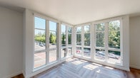 Located at 4015 Mercantile Dr in Lake Oswego, Oregon, this modern single-floor residence is defined by its bright, contemporary design and thoughtful finishes throughout. The living area is a true standout, featuring an expansive corner window wall with floor-to-ceiling glass panes that flood the space with natural light and offer sweeping views of the surrounding neighborhood and lush Pacific Northwest tree canopy. The herringbone-patterned hardwood flooring runs throughout the main living areas, adding a refined, geometric elegance to the open layout. A wall-mounted mini-split unit ensures year-round climate comfort. The kitchen is well-appointed with two-tone cabinetry — crisp white upper cabinets paired with deep charcoal lowers — complemented by gold hardware, a white subway tile backsplash, stone countertops, and a suite of stainless steel appliances including a gas range. Open shelving adds functional style. The bathroom features clean white finishes, a dark-toned vanity with a stone countertop, a large mirror, and warm pendant lighting. An additional room with a dedicated window offers views of the surrounding streetscape and neighboring buildings, providing a versatile space adaptable to various needs.