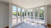 Located at 4015 Mercantile Dr in Lake Oswego, Oregon, this modern single-floor residence is defined by its bright, contemporary design and thoughtful finishes throughout. The living area is a true standout, featuring an expansive corner window wall with floor-to-ceiling glass panes that flood the space with natural light and offer sweeping views of the surrounding neighborhood and lush Pacific Northwest tree canopy. The herringbone-patterned hardwood flooring runs throughout the main living areas, adding a refined, geometric elegance to the open layout. A wall-mounted mini-split unit ensures year-round climate comfort. The kitchen is well-appointed with two-tone cabinetry — crisp white upper cabinets paired with deep charcoal lowers — complemented by gold hardware, a white subway tile backsplash, stone countertops, and a suite of stainless steel appliances including a gas range. Open shelving adds functional style. The bathroom features clean white finishes, a dark-toned vanity with a stone countertop, a large mirror, and warm pendant lighting. An additional room with a dedicated window offers views of the surrounding streetscape and neighboring buildings, providing a versatile space adaptable to various needs.