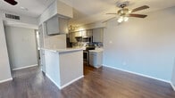 This single-story, 1-bedroom, 2-bathroom unit offers a practical and modern layout designed to maximize its compact footprint. The open-concept main living area seamlessly integrates the dining room, kitchen, and living room into one cohesive space. Dark hardwood-style flooring runs throughout, providing a warm contrast to the cool gray walls and white trim found across every room.

The kitchen is a standout feature, equipped with stainless steel appliances including a range, microwave, refrigerator, and dishwasher. Gray cabinetry pairs with light granite-style countertops and a mosaic tile backsplash for a contemporary aesthetic. A peninsula counter adds additional prep space and visual separation from the living area.

The living room benefits from natural light via a set of glass double doors fitted with blinds, and is equipped with a ceiling fan with light fixture — a detail echoed in the bedroom as well. The bedroom is a comfortable, well-proportioned space with a window allowing in natural light, a closet for storage, and access to one of the two bathrooms.

Both bathrooms are clean and functional. One features a vanity with a granite-style countertop and framed mirror, while the other includes a full bathtub and shower combination. Additional storage is provided by a dedicated pantry. A hallway connects the rooms efficiently, completing this well-organized layout.