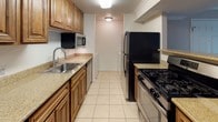 This single-floor residence offers a well-organized layout with two bedrooms and two full bathrooms. The living area is bright and open, featuring wood-look luxury vinyl plank flooring, crown molding, and neutral warm-toned walls. A sliding glass door floods the space with natural light while providing outdoor views, complemented by a dedicated entry door for added convenience.

The galley-style kitchen is efficiently designed with warm wood cabinetry, granite-look countertops, a double stainless steel sink, and a full suite of appliances including a gas range, refrigerator, microwave, and dishwasher. Light tile flooring runs throughout the kitchen. A breakfast bar connects the kitchen to the living and dining areas, enhancing the open feel.

Both bedrooms are carpeted and receive natural light through windows with outdoor views. Crown molding is present in the primary bedroom, adding a refined touch. Each bedroom is served by its own full bathroom. Both bathrooms feature tile flooring, wood vanities with granite-look countertops, and a tub/shower combination—one with frosted glass sliding doors and one with classic white tile surround.