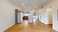 This two-story home presents a clean, contemporary design characterized by neutral tones, recessed lighting, and an efficient use of space throughout both levels. The main floor centers around an open-concept living and kitchen area, where light hardwood flooring runs continuously, creating a seamless and airy feel. A large picture window at the front of the living area admits generous natural light and offers street views, while a frosted glass interior door adds a modern design touch.

The kitchen is well-equipped with medium-toned wood cabinetry extending to the ceiling for ample storage, granite countertops, a full suite of stainless steel appliances including a refrigerator, range, microwave, and dishwasher, and a central island providing additional prep space. A window above the sink further brightens the workspace. A compact half bath with a pedestal sink is also found on the main level.

Upstairs, carpeted bedrooms offer a quieter, comfortable retreat, each featuring recessed lighting and windows dressed with roller shades. A full bathroom with a tub-shower combination serves the upper level. Throughout, the home maintains a consistent, modern aesthetic with white walls and clean finishes.