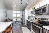 Located at 335 Cedar St in Waterloo, Iowa, this thoughtfully designed one-bedroom, one-bathroom unit maximizes every square foot with a smart, efficient floor plan. The open-concept kitchen and living area form the heart of the space, featuring light wood-tone flooring, white cabinetry, a classic subway tile backsplash, and a full suite of stainless steel appliances including a refrigerator, electric range, microwave, and dishwasher. A built-in countertop ledge provides additional prep or dining space, adding to the kitchen's functionality. The living area is bathed in natural light through large floor-to-ceiling windows and a glass sliding door that opens onto a private balcony, offering open views of the surrounding Waterloo cityscape. Clean white walls and contemporary track lighting contribute to the bright, modern ambiance throughout. The cozy bedroom accommodates a full-sized bed comfortably, with a window that brings in additional natural light and creates an airy feel. The bathroom is finished with large-format light tile flooring and connects to a hallway that also houses a stacked washer and dryer unit — a practical in-unit amenity. Throughout the space, the design aesthetic is clean, modern, and efficient, making it a well-appointed urban residence.