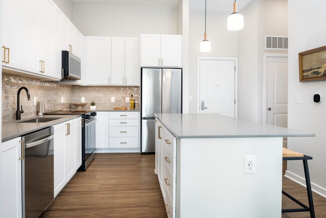 Colección de diseño I Cocina con gabinetes blancos, salpicadero de azulejos beige, encimeras de cuarzo gris, iluminación colgante y pisos de superficie dura - Avalon Annapolis