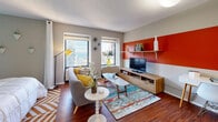 Located at 441 East Erie Street in Chicago's Streeterville neighborhood, this efficiently designed unit makes excellent use of its single-floor layout. Rich hardwood floors run throughout the main living areas, providing a warm contrast to the bold, colorful accent walls in orange and aqua that define the space's eclectic, mid-century modern aesthetic.

The open living area is bright and inviting, featuring two windows with sweeping city views, including glimpses of the Chicago skyline. A built-in media shelf with an orange accent wall anchors the entertainment zone, while the layout comfortably accommodates both a seating and a workspace area.

The kitchen is accessible via a raised breakfast bar with stylish bar seating, offering a functional pass-through that keeps the space feeling open and connected. A full suite of appliances, including a stainless steel range, is visible from the main living area.

The sleeping alcove is separated by a curtain partition, offering privacy while maintaining the unit's open feel. It features vibrant teal-painted walls, a generous built-in closet with ample shelving, and hardwood flooring.

The full bathroom is cleanly finished with large-format tile on the walls and floors, a soaking tub with shower combination, a wood-framed mirror, and a granite-topped vanity. A textured ceiling is consistent throughout the unit, adding architectural character to this thoughtfully styled Chicago residence.