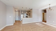 This single-floor residence showcases a clean, contemporary design with a neutral palette of soft grey tones, white trim, and light wood-look flooring that flows seamlessly throughout the space. The open-concept kitchen is a standout feature, equipped with stainless steel appliances including a refrigerator, range, and microwave, complemented by sleek grey cabinetry, white quartz countertops, and a central peninsula with an undermount sink and dishwasher. Elegant pendant lighting above the peninsula adds a refined touch, while recessed lighting provides consistent illumination. The kitchen opens directly into a spacious living and dining area, which benefits from abundant natural light through multiple windows fitted with white blinds. A chandelier anchors the dining zone, while a ceiling fan enhances comfort in the living area. The bedrooms are generously sized, each featuring light flooring, ceiling fans or pendant lighting, and large windows that invite natural light. One bedroom includes a walk-in closet outfitted with wire shelving and hanging rods for ample storage. The full bathroom is well-designed with a dual-sink grey vanity, white quartz countertop, soaking tub, and a separate tiled walk-in shower, all finished with brushed gold hardware accents.