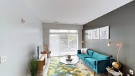 This single-floor residence combines modern design with functional living across several well-defined spaces. The living room serves as a welcoming focal point, featuring large sliding glass doors that flood the room with natural light and provide views of the outdoors. A bold accent wall in dark grey anchors the space, complementing the light flooring that runs throughout the common areas.

The kitchen is thoughtfully designed with rich dark-wood cabinetry, white countertops, and a full suite of black appliances, including a refrigerator, range, microwave, and dishwasher. A butcher-block island with seating provides a casual dining option, while pendant lighting and track lights enhance both style and functionality. Ample upper and lower cabinet storage adds practicality.

The two bedrooms are carpeted and naturally lit through window blinds, offering a quiet, comfortable atmosphere. Each has access to its own bathroom, both finished with dark-wood vanities, white countertops, and wood-look flooring. One bathroom features a shower-tub combination, while the other includes a tub with a striped curtain.

A dedicated utility closet houses a stacked washer and dryer alongside a water heater, providing convenient in-unit laundry. The overall aesthetic is cohesive, modern, and practical.