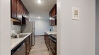 This single-floor unit offers a practical and thoughtfully designed layout, encompassing a combined kitchen and living area along with a full bathroom. The galley-style kitchen is a standout feature, boasting rich dark-wood cabinetry with brushed hardware, light granite countertops, and a full suite of stainless steel appliances including a refrigerator, electric range, and dishwasher. A textured ceiling and recessed lighting add dimension overhead, while light wood-style flooring runs throughout, creating a cohesive and clean aesthetic.

The living area is open and versatile, bathed in natural light from a large window dressed with vertical blinds. The neutral gray walls provide a calm, move-in-ready backdrop, and a baseboard heating unit ensures year-round comfort. The space flows easily from the kitchen, making it well-suited for both everyday living and entertaining.

The bathroom continues the consistent design language of the unit, featuring a dark wood vanity with a white countertop and integrated sink, a large frameless mirror, and matching cabinetry above for added storage. The overall ambiance of this space is clean, modern, and functional, with cohesive finishes tying each area together seamlessly.