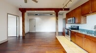 This one-bedroom, two-bathroom loft-style unit at 427 Pershing Ave in Davenport, Iowa, blends historic industrial character with modern finishes across a well-planned single-floor layout. The open living area is defined by rich hardwood flooring, exposed original timber columns and beams, and industrial-style ductwork running across the ceiling, lending the space a distinctive warehouse aesthetic. Track lighting and a ceiling fan complete the look overhead.

The kitchen features warm cherry wood cabinetry, granite countertops, a full suite of stainless steel appliances including a range, microwave, and dishwasher, and tile flooring. An exposed brick accent wall adds texture and charm to the cooking space.

The bedroom continues the hardwood flooring and showcases another exposed brick wall with an arched window that brings in natural light and views of the surrounding area. Original timber beams frame the room, and a dedicated closet provides convenient storage.

Both bathrooms are finished with marble-style tile on the floors and in the tub surround, complemented by warm wood vanities with granite countertops. An in-unit stacked washer and dryer adds everyday convenience. The unit offers a compelling mix of historic architectural detail and contemporary amenities throughout.