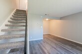 This two-story residence offers a well-designed layout that balances functionality and comfort across both levels. The entry level welcomes you with durable wood-look flooring that flows throughout the main living areas. A carpeted staircase with sleek black metal railings connects the two floors, adding a modern touch to the interior. The lower level features an open living area with recessed accent lighting and a neutral color palette that creates a clean, airy atmosphere, complemented by a textured ceiling throughout.

The kitchen is efficiently designed with crisp white shaker-style cabinetry, granite-look countertops, a stainless steel sink and dishwasher, and a full suite of appliances including a range and refrigerator. The wood-look flooring continues here, reinforcing a cohesive aesthetic.

Upstairs, plush blue carpet covers the main bedroom area, which receives natural light through a large window fitted with vertical blinds. The upper level also includes a carpeted secondary room with built-in closet shelving, providing excellent storage. A full bathroom with a tub-shower combination, chrome fixtures, and a curved shower rod completes the upper floor. Throughout both levels, clean white baseboards and neutral gray walls contribute to a fresh, move-in-ready presentation.