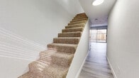 This two-story space is designed with a clean, contemporary aesthetic, featuring light wood-style luxury vinyl plank flooring that runs consistently throughout, complementing the bright white walls and trim. The ground floor includes an open living area bathed in natural light from a full-width sliding glass door that opens to a private fenced outdoor space, offering a seamless indoor-outdoor connection.

The galley-style kitchen is efficiently laid out with white shaker cabinetry lining both sides, light countertops, a stainless steel sink with a gooseneck faucet, and stainless steel appliances including a refrigerator, dishwasher, and electric range with overhead ventilation. A separate water closet provides a private toilet area on one of the floors.

The staircase, carpeted in plush beige, connects the two levels and is positioned adjacent to a hallway leading to the rear sliding door. Upstairs, the bedrooms feature the same light flooring and neutral walls. One bedroom includes dual built-in closets with bifold doors, offering generous storage. A bathroom with white cabinetry, a vanity, and a tiled soaking tub completes the upper level. Throughout, recessed and flush-mount lighting maintains a bright, well-illuminated environment.