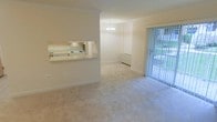 This single-floor residence offers a clean, open layout filled with natural light. The living and dining areas are finished with plush wall-to-wall carpeting in a neutral tone, creating a comfortable and cohesive feel throughout. Crown molding adds a refined architectural touch to the space.

The kitchen features a convenient pass-through window that opens directly into the dining area, promoting an open and connected atmosphere. The kitchen is equipped with a white range and oven, under-cabinet lighting, and light-colored cabinetry, maintaining a bright and functional workspace.

The dining area is highlighted by an elegant chandelier that serves as a focal point, adding a touch of classic charm to the space. Adjacent to the living area, a large sliding glass door fitted with vertical blinds allows abundant natural light to fill the room while providing direct access to an outdoor area, where greenery is visible beyond the glass.

The overall ambiance of the space is light, airy, and welcoming, with a consistent neutral color palette across the walls, trim, and flooring. The thoughtful layout and architectural details make this a practical yet inviting single-floor home.