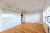 Located at 111 Lawton Blvd in the desirable Forest Hill neighbourhood of Toronto, this efficiently designed studio presents a clean, contemporary aesthetic throughout. Warm honey-toned hardwood flooring extends across the entire living area, complementing the bright white walls and recessed pot lighting that keep the space feeling open and airy.

The living area is anchored by a generous picture window offering elevated views of the Toronto skyline and surrounding greenery, flooding the room with natural light. A sleek built-in kitchenette is tucked neatly into its own alcove, outfitted with flat-panel white cabinetry extending to the ceiling, a light blue glass backsplash, an integrated sink, and a compact cooking surface — maximizing both function and visual tidiness. Frosted glass sliding doors provide elegant storage or room division nearby.

A narrow hallway with recessed lighting connects the main living space to the bathroom, which is finished to a high standard. Large-format beige tiles line the floors and walls, while a glass-enclosed walk-in shower with a rain showerhead serves as the centrepiece. A floating white vanity and full mirror complete the refined, spa-like feel. The overall design of the space prioritizes clean lines, smart storage, and a neutral palette, creating a polished and functional urban retreat.