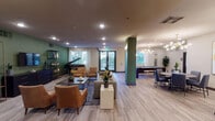 This thoughtfully designed single-floor community amenity space offers a diverse range of gathering and recreational areas to accommodate a variety of resident needs. The centerpiece is a spacious open lounge area anchored by a grand piano, complemented by an arrangement of leather and upholstered seating, light wood-plank flooring, and green accent columns that add architectural character. Large windows allow natural light to fill the space, while recessed lighting and an elegant chandelier illuminate the billiards and dining zones nearby. A dedicated library nook features floor-to-ceiling industrial shelving stocked with books and board games, paired with comfortable lounge seating beneath a sculptural sputnik chandelier. A cozy media room offers a large wall-mounted TV, bold abstract artwork, and refined furnishings beneath a gold globe chandelier. The community dining area includes multiple long tables with leather chairs, a wet bar counter, and a wall-mounted TV for shared gatherings. A fully equipped kitchen with stainless steel appliances, modern cabinetry, and white countertops supports event preparation. Additional amenities include a well-stocked laundry facility with multiple washers and dryers, a private wellness or treatment room, and an elegantly appointed round-table meeting area accented by vibrant wall art and a statement chandelier.