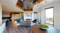 Located in Oakland, CA (94608), this elegantly designed single-floor communal amenity space offers a refined and welcoming environment for gathering and leisure. The open-plan lounge is anchored by a sleek, marble-surround fireplace topped with a wall-mounted flat-screen TV, creating an inviting focal point for relaxation. Plush seating arrangements — including a gray sectional sofa, tufted blue accent chairs, and curved upholstered armchairs — are thoughtfully arranged across large-format slate tile flooring, lending warmth and sophistication to the space.

The ceiling is a striking architectural feature, combining a dark tray section with warm wood accents and an elaborate array of pendant lighting, including cascading cylindrical pendants and track lighting, casting a warm, ambient glow throughout. Floor-to-ceiling windows along one wall flood the interior with abundant natural light and provide views to an adjoining outdoor terrace, accessible via a set of glass-panel doors.

A dedicated wet bar area is outfitted with warm wood cabinetry, a stone countertop peninsula with bar seating, a wine refrigerator, and marble-tiled walls, making it well-suited for entertaining. Curated artwork and a reception-style counter near the entry contribute to the polished, hotel-like ambiance of this contemporary community space.