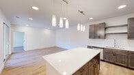 This single-floor space showcases a contemporary design with a cohesive palette of light hardwood flooring, crisp white walls, and dark-toned cabinetry that runs throughout. The open-concept kitchen serves as a central highlight, equipped with rich espresso-finish cabinetry, a white quartz countertop island, a classic subway tile backsplash, and a full suite of stainless steel appliances including a range, microwave, dishwasher, and refrigerator. Cylindrical pendant lights hang above the island, providing focused task lighting while adding a modern aesthetic detail. The kitchen flows seamlessly into a generous living area, creating an inviting, flexible space for daily use.

A long, well-lit hallway connects the private areas of the unit, lined with recessed ceiling lights and panel-style doors. The bedrooms are bright and airy, featuring recessed lighting, large windows that bring in natural light, and built-in closets. One bedroom features sliding glass doors opening directly onto a private outdoor deck with wooded views beyond. A full bathroom includes a dual-sink vanity with quartz countertops, dark cabinetry, and a soaking tub with shower combination. Additional storage space and a dedicated laundry area complete the thoughtfully arranged layout.