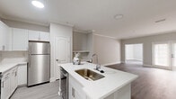 Located on Cheshire Bridge Road NE in Atlanta, GA, this two-bedroom, one-bathroom residence offers a well-designed single-level layout with a clean, modern aesthetic throughout. The open-concept kitchen and living area serves as the heart of the home, featuring a large quartz-topped island with an undermount sink, crisp white shaker cabinetry extending to the ceiling, a tile backsplash, and a full suite of stainless steel appliances including a refrigerator, range, microwave, and dishwasher. The living room flows naturally from the kitchen and is anchored by elegant crown molding and neutral warm-gray walls, with French doors that invite natural light into the space. Consistent wood-look flooring runs throughout the entire home, lending a cohesive and contemporary feel. The primary bedroom is a generously sized retreat, complemented by a dedicated walk-in closet outfitted with wire shelving and hanging rods for organized storage. The second bedroom also includes a closet and offers a bright, open atmosphere. The bathroom is finished in a clean, neutral palette with a white vanity featuring quartz countertops, a framed mirror, and a full tub-shower combination. A hallway connects the private areas of the home, completing the functional and thoughtfully arranged floor plan.