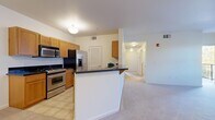 This single-floor residence offers a practical and comfortable layout across two bedrooms and one bathroom. The open-concept kitchen and living area serves as the heart of the home, featuring warm honey-toned cabinetry, dark granite countertops, and a full suite of stainless steel appliances including a gas range, built-in microwave, refrigerator, and dishwasher. A peninsula with a dark countertop provides additional prep space and defines the transition between the kitchen and living area. Light tile flooring runs through the kitchen, while durable wood-look planks extend throughout the main living and bedroom areas, adding warmth and visual continuity. The living room benefits from a sliding door that opens to an outdoor space, allowing natural light to fill the area. The primary bedroom includes a ceiling fan and its own closet, while the secondary bedroom is finished with soft carpeting. The bathroom is well-appointed with a wood-toned vanity, dark granite countertop, large mirror, and tile flooring. A dedicated entrance and an additional closet with built-in shelving provide practical storage solutions. The unit's clean white walls and recessed lighting contribute to a bright, neutral ambiance throughout.