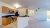 This single-floor residence offers a practical and comfortable layout across two bedrooms and one bathroom. The open-concept kitchen and living area serves as the heart of the home, featuring warm honey-toned cabinetry, dark granite countertops, and a full suite of stainless steel appliances including a gas range, built-in microwave, refrigerator, and dishwasher. A peninsula with a dark countertop provides additional prep space and defines the transition between the kitchen and living area. Light tile flooring runs through the kitchen, while durable wood-look planks extend throughout the main living and bedroom areas, adding warmth and visual continuity. The living room benefits from a sliding door that opens to an outdoor space, allowing natural light to fill the area. The primary bedroom includes a ceiling fan and its own closet, while the secondary bedroom is finished with soft carpeting. The bathroom is well-appointed with a wood-toned vanity, dark granite countertop, large mirror, and tile flooring. A dedicated entrance and an additional closet with built-in shelving provide practical storage solutions. The unit's clean white walls and recessed lighting contribute to a bright, neutral ambiance throughout.