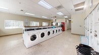 Located at 7650 Highlands View Rd in Truckee, California, this well-appointed community laundry facility offers a generous, single-floor layout designed for convenience and functionality. The space is organized efficiently, with a long row of front-loading washing machines paired with stacked dryers lining the walls, providing ample capacity for simultaneous use. The interior features a drop ceiling with recessed fluorescent lighting that ensures the room is consistently bright and well-illuminated throughout. Light-toned tile flooring extends across the entire space, contributing to a clean and easy-to-maintain environment. A standout feature is the stainless steel pet washing station, complete with a ramp and spray attachment, catering to the needs of pet owners. Multiple windows fitted with horizontal blinds allow natural light to filter in, adding to the room's open and airy feel. A vibrant teal accent wall adds a touch of color and visual interest to the otherwise neutral palette. Bulletin boards mounted on the walls provide space for community notices and information. Snack and beverage vending machines are conveniently situated near the exit, enhancing the facility's practicality. A dedicated utility sink rounds out the functional amenities, making this laundry facility a comprehensive and user-friendly resource for the community.