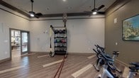 Located at 5501 Old Montgomery Hwy in Tuscaloosa, Alabama, this single-floor fitness studio is a well-appointed exercise facility designed to support a wide range of workout styles. The space features durable hardwood-style flooring with light accent inlays, neutral-toned walls with dark crown molding, and multiple ceiling fans paired with recessed lighting to maintain a comfortable environment during workouts.

The studio is organized into distinct functional zones. A dedicated cardio area houses a row of spin bikes, ideal for cycling sessions and group fitness classes. Opposite this area, a multi-tiered equipment rack stores a full assortment of kettlebells, medicine balls, and resistance accessories including TRX suspension trainers with yellow straps. Battle ropes are laid out across the floor, signaling a space built for high-intensity interval training. A built-in storage bench along one wall provides convenient space for yoga balls and other accessories.

Natural light enters through multiple windows fitted with white horizontal blinds, and artwork depicting nature scenes adds a welcoming aesthetic touch. A wall-mounted flat-screen television is positioned for visibility across the open floor, supporting guided workout programming. The open layout allows for ample movement and flexibility, accommodating both individual and group training sessions with ease.