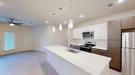 Located in Manor, TX, this well-designed 2-bedroom, 2-bathroom residence offers a thoughtfully planned single-level layout with a clean, contemporary aesthetic throughout. The open-concept living and kitchen area forms the heart of the home, anchored by a large white quartz kitchen island with an undermount sink and striking pendant lighting overhead. The kitchen features crisp white upper cabinetry, rich dark wood lower cabinets, a classic subway tile backsplash, and a full suite of stainless steel appliances. Light wood-tone flooring flows seamlessly throughout the entire space, enhancing the bright and airy atmosphere created by recessed lighting and natural light. The living area is spacious and comfortable, equipped with a ceiling fan and French doors that open to an outdoor view, filling the room with natural light. Both bedrooms are generously sized, each with a ceiling fan, large windows, and dedicated closet space. The primary bedroom is notably spacious and connects to its own bathroom. The two bathrooms feature wood-toned cabinetry with white countertops, tiled tub-shower combinations, and coordinating brushed nickel hardware, maintaining the modern and cohesive design palette found throughout this well-appointed residence.