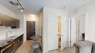 Located on the vibrant King Street corridor in Charleston, SC, this one-bedroom, one-bathroom unit offers a thoughtfully designed layout that maximizes every square foot. The open kitchen anchors the living area and features dark-toned cabinetry with sleek hardware, white subway tile backsplash, light wood-look flooring, and a full suite of stainless steel appliances including a refrigerator, range, built-in microwave, and dishwasher. Track lighting overhead adds a modern, industrial touch. A compact dining area with a round bistro table sits just off the kitchen, creating a natural flow toward the entryway. Notably, in-unit laundry is tucked conveniently behind a paneled door. The bedroom is a cozy, well-lit retreat with neutral wall tones, plush carpeting, and multiple windows fitted with horizontal blinds that allow natural light to filter in. A skylight adds an additional source of brightness overhead. The bathroom is finished with tile flooring, a granite-topped vanity with dark wood cabinetry, a framed mirror, and a walk-in shower with wood-toned surround. Clean lines and neutral tones throughout give the unit a cohesive, contemporary feel suited for urban living in the heart of Charleston.