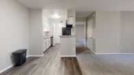 Located at 5300 Glenside Dr in Henrico, Virginia, this single-floor residence offers a well-organized layout designed for comfortable everyday living. The living room serves as the heart of the home, featuring plush carpeting, neutral taupe walls, and a classic brick-surround fireplace flanked by a window with vertical blinds that invite natural light into the space. Adjacent to the living area, the kitchen is equipped with white cabinetry, granite-style countertops, stainless steel appliances including a refrigerator and dishwasher, and a central peninsula that provides additional prep space and separates the kitchen from the main living and hallway areas. Wood-look vinyl plank flooring runs throughout the kitchen and entry zones, creating a clean transition between spaces. The bedrooms are carpeted and finished in warm neutral tones, each featuring windows with blinds that provide views of the surrounding greenery, and one bedroom includes a closet with a paneled door. Two bathrooms are present in the unit, both featuring wood-look flooring, tiled tub-shower combinations, toilets, and white vanities with contemporary hardware. The overall aesthetic is clean, neutral, and move-in ready, with consistent finishes throughout that lend the space a cohesive and functional character.
